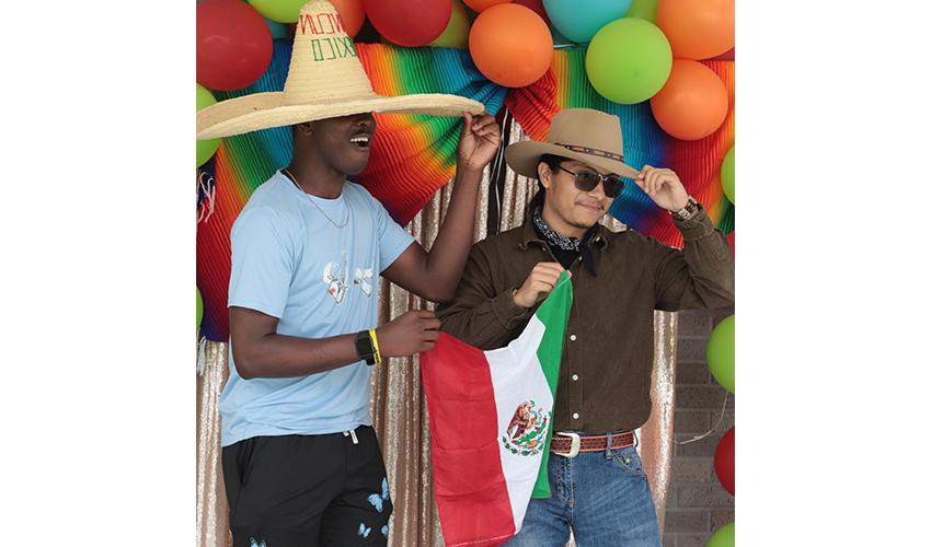 Two students taking a picture with the Mexico flag and their sombreros. 
